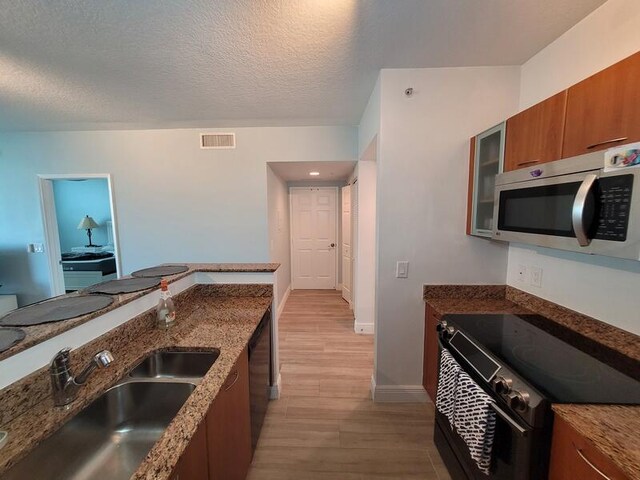 kitchen featuring dark stone counters, black electric range oven, light hardwood / wood-style flooring, a textured ceiling, and sink