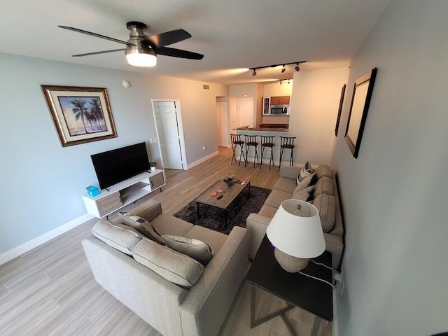 living room featuring rail lighting, ceiling fan, and light wood-type flooring