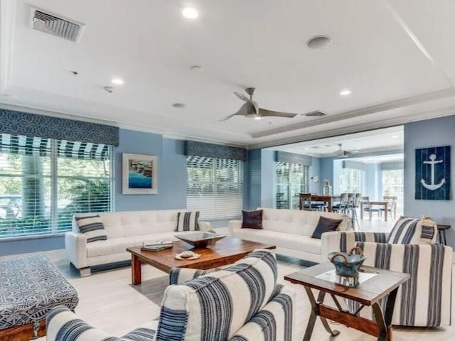 living room with ceiling fan, light wood-type flooring, and a raised ceiling