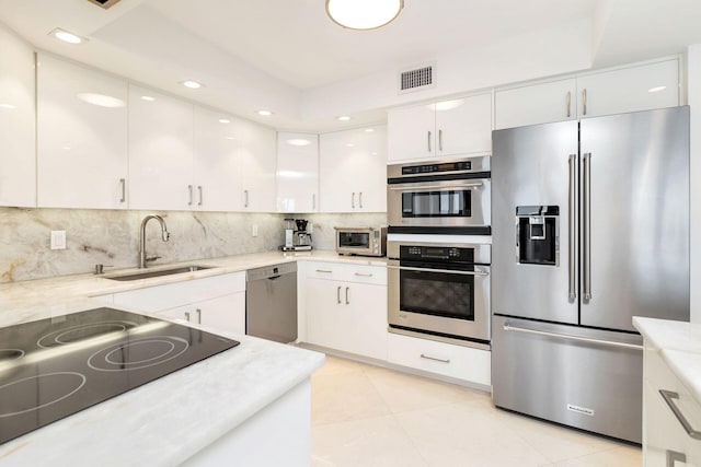 kitchen with appliances with stainless steel finishes, white cabinetry, backsplash, sink, and light tile flooring