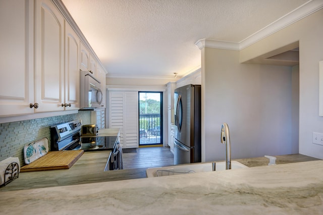 kitchen featuring backsplash, white cabinetry, stainless steel appliances, ornamental molding, and hardwood / wood-style flooring