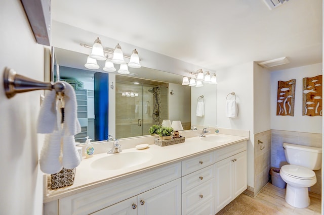 bathroom with tile walls, oversized vanity, toilet, an enclosed shower, and dual sinks