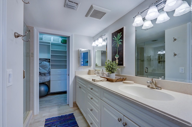 bathroom with a shower with door, hardwood / wood-style floors, vanity with extensive cabinet space, and double sink