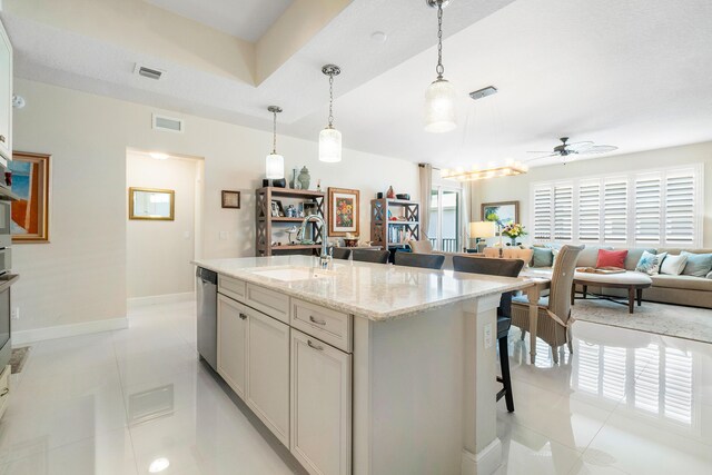 kitchen with sink, a center island with sink, light tile patterned floors, ceiling fan, and light stone countertops