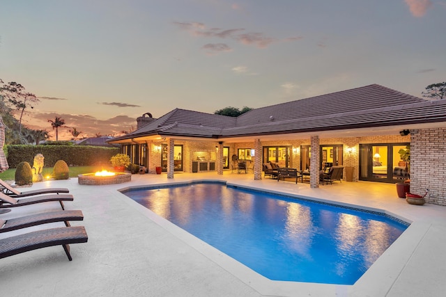 pool at dusk featuring a patio area and an outdoor living space with a fire pit