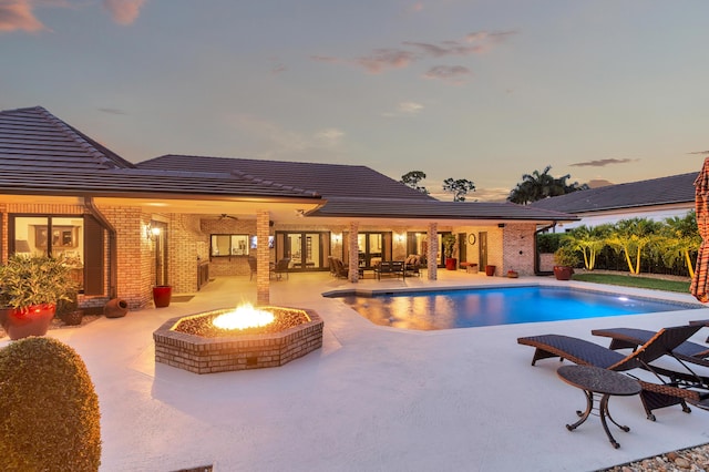 pool at dusk featuring a fire pit and a patio