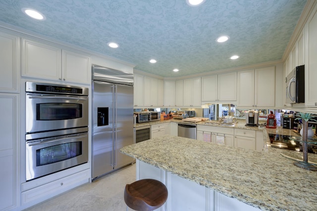 kitchen featuring white cabinetry, stainless steel appliances, kitchen peninsula, a textured ceiling, and a kitchen bar