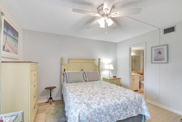 bedroom with a textured ceiling, ceiling fan, light hardwood / wood-style floors, and connected bathroom