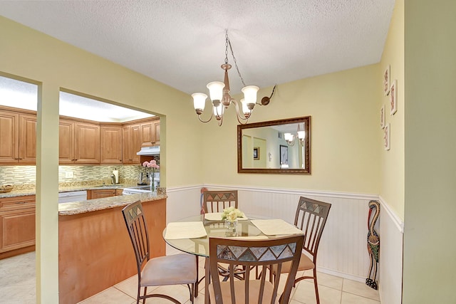 tiled dining room featuring a textured ceiling, sink, and an inviting chandelier