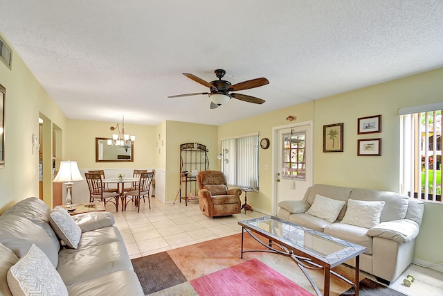 living room with ceiling fan with notable chandelier, a textured ceiling, and light tile flooring