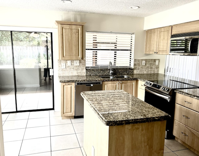 kitchen featuring sink, a center island, dark stone counters, a textured ceiling, and appliances with stainless steel finishes