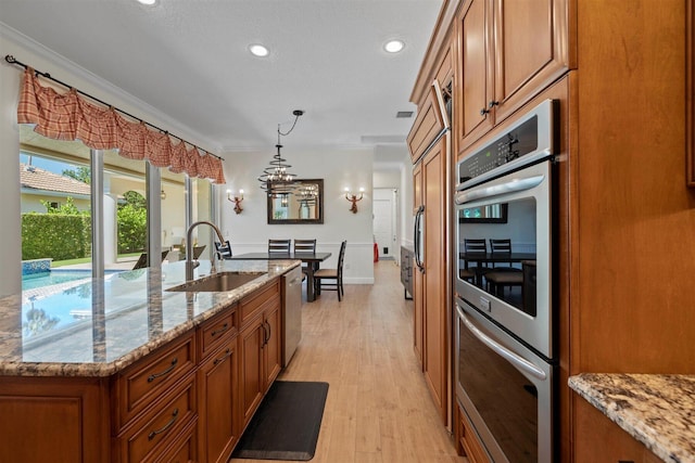 kitchen with an inviting chandelier, stainless steel appliances, light hardwood / wood-style flooring, and light stone counters