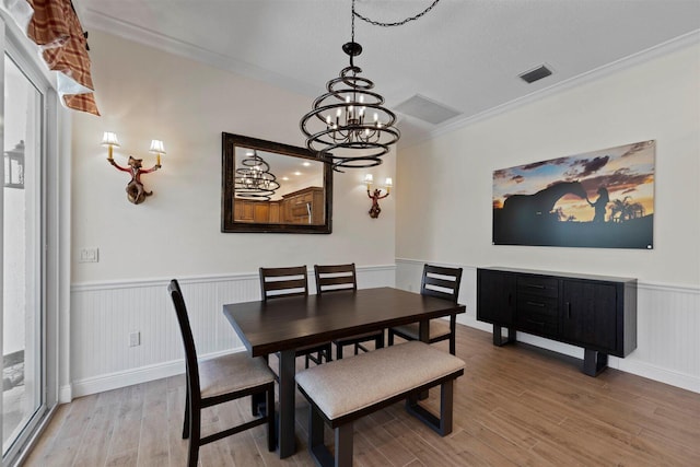 dining space featuring light hardwood / wood-style floors, ornamental molding, a textured ceiling, and a chandelier