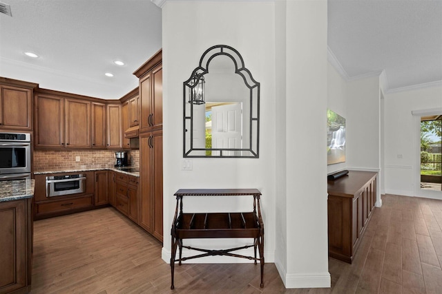 kitchen featuring dark stone counters, wood-type flooring, backsplash, custom exhaust hood, and crown molding