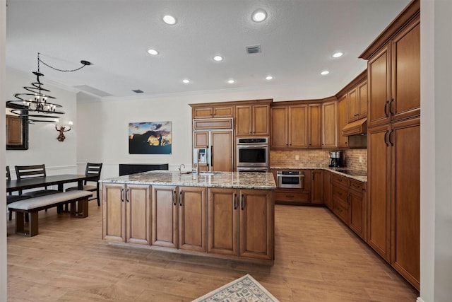 kitchen with an island with sink, light hardwood / wood-style floors, light stone countertops, tasteful backsplash, and ornamental molding