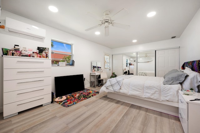 bedroom with a wall mounted air conditioner, light wood-type flooring, ceiling fan, and a closet