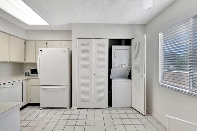 kitchen with cream cabinetry, a textured ceiling, white appliances, light tile patterned flooring, and stacked washer and clothes dryer