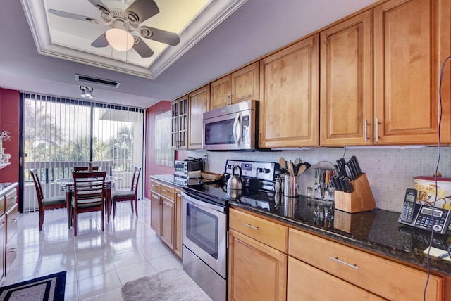 kitchen with light tile flooring, stainless steel appliances, a raised ceiling, dark stone counters, and ceiling fan