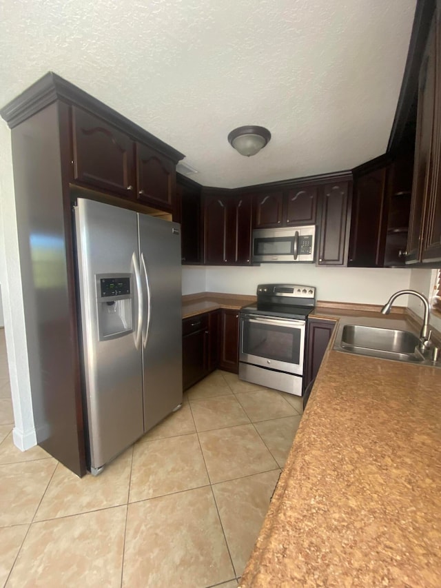 kitchen featuring sink, light tile patterned floors, a textured ceiling, dark brown cabinets, and stainless steel appliances