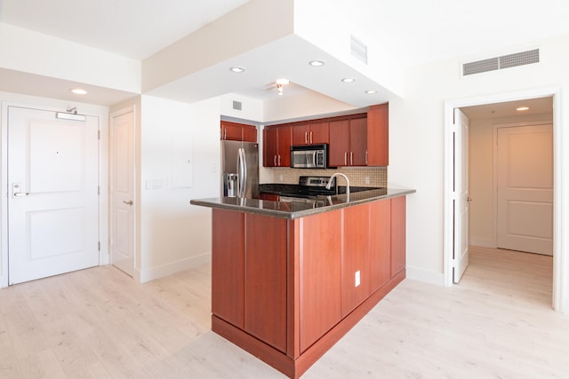 kitchen with tasteful backsplash, kitchen peninsula, light hardwood / wood-style floors, and appliances with stainless steel finishes