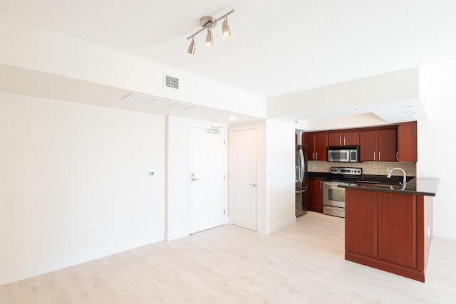 kitchen with appliances with stainless steel finishes, rail lighting, kitchen peninsula, light wood-type flooring, and backsplash