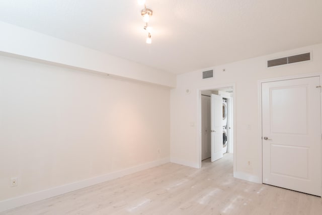 unfurnished room featuring stacked washer and clothes dryer, light hardwood / wood-style floors, and track lighting