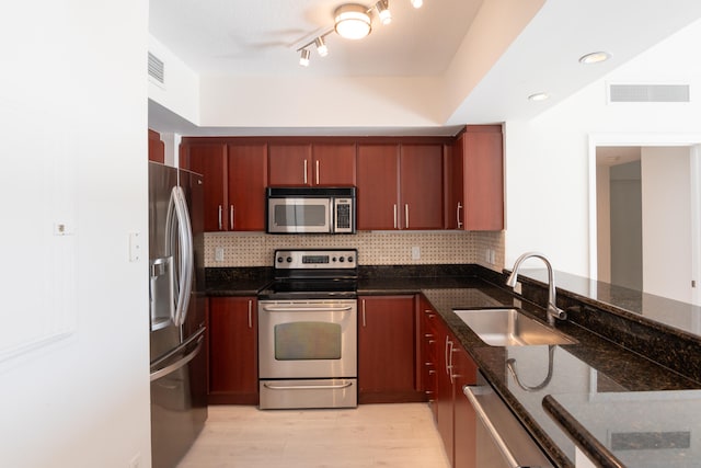 kitchen with dark stone counters, appliances with stainless steel finishes, track lighting, light wood-type flooring, and sink