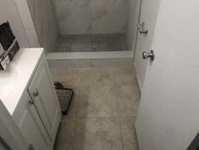 bathroom with tile flooring, tiled shower, and vanity