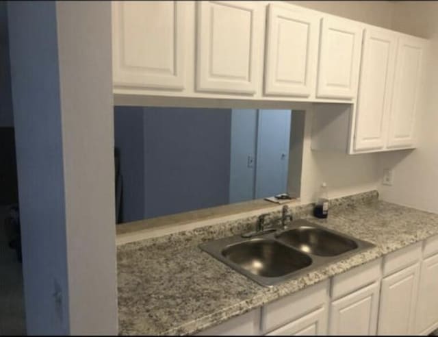 kitchen featuring white cabinets, light stone counters, and sink