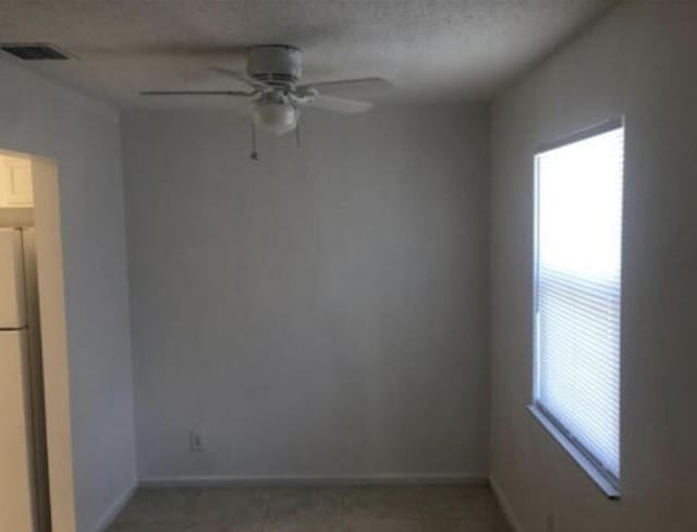 empty room with plenty of natural light, dark tile floors, and ceiling fan