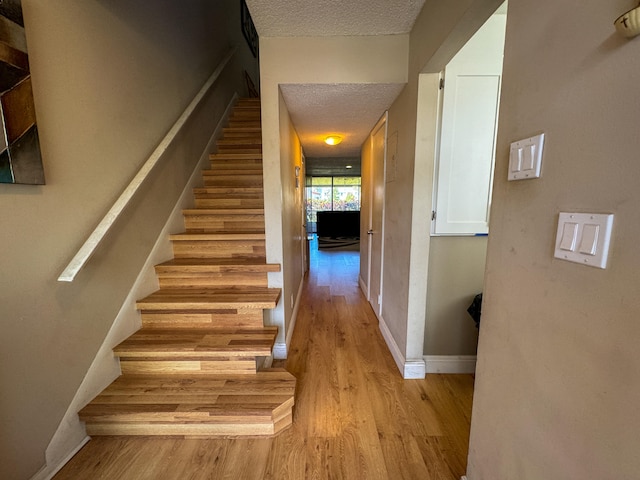 stairs with light hardwood / wood-style floors and a textured ceiling