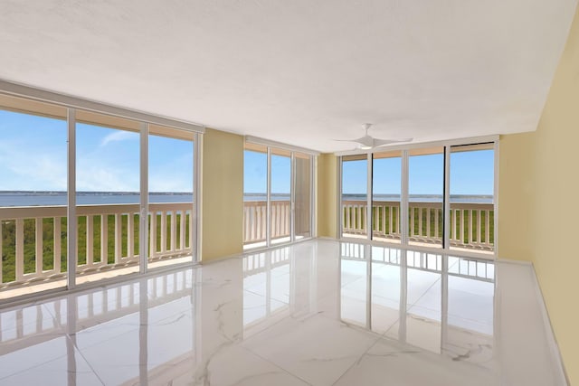 unfurnished room with a water view, marble finish floor, ceiling fan, and floor to ceiling windows