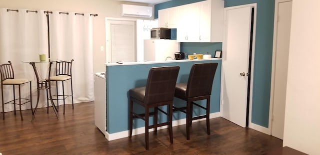 interior space with dark wood-type flooring, a breakfast bar, white refrigerator, white cabinets, and a wall unit AC