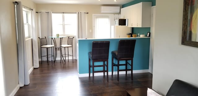 kitchen with a breakfast bar area, dark hardwood / wood-style flooring, white cabinets, and an AC wall unit