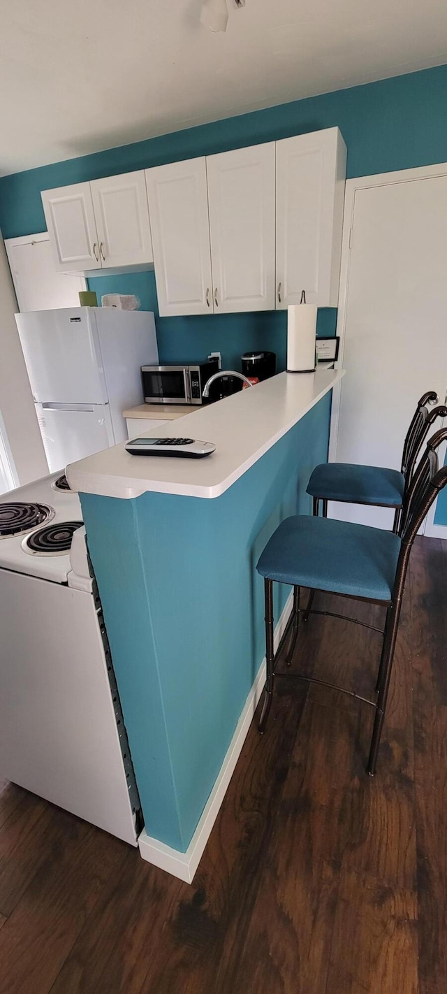 kitchen featuring white cabinets, white fridge, dark wood-type flooring, and a breakfast bar