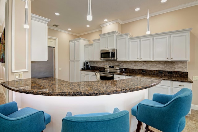 kitchen with appliances with stainless steel finishes, hanging light fixtures, dark stone counters, and white cabinetry