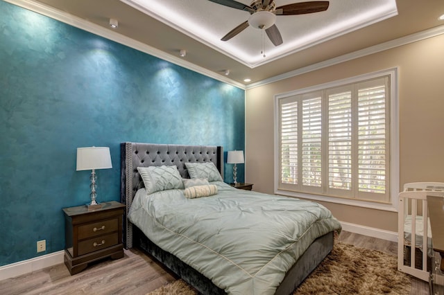 bedroom with hardwood / wood-style floors, ceiling fan, a tray ceiling, and multiple windows