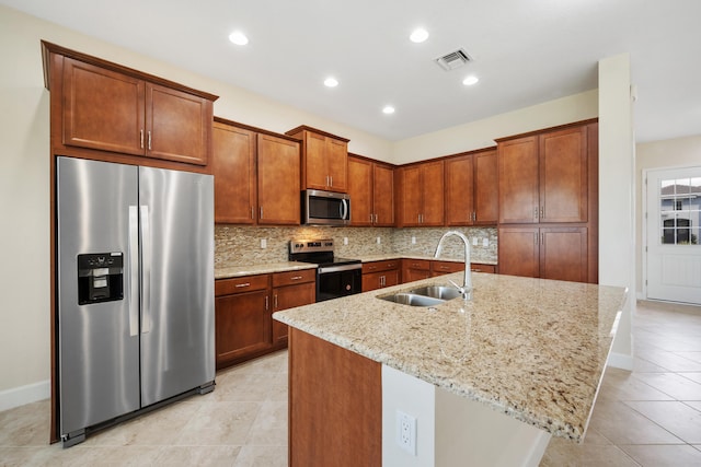 kitchen featuring light stone countertops, light tile flooring, appliances with stainless steel finishes, a center island with sink, and tasteful backsplash