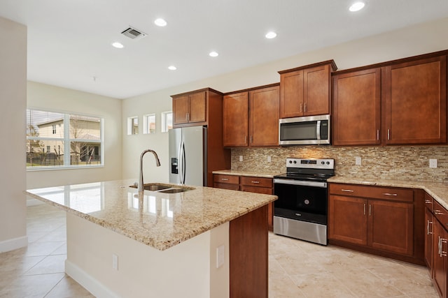 kitchen featuring backsplash, a kitchen island with sink, appliances with stainless steel finishes, and light stone counters