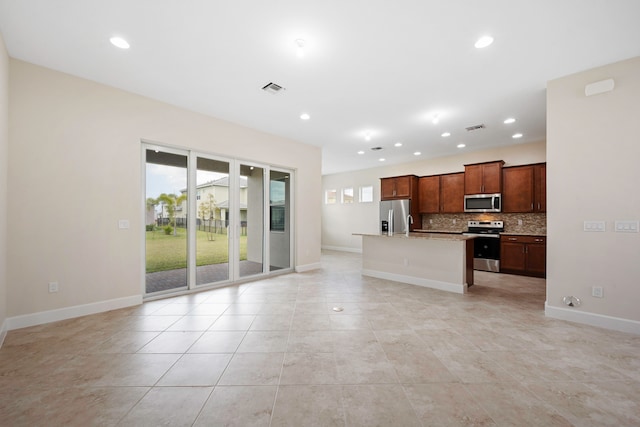 kitchen featuring light tile floors, appliances with stainless steel finishes, backsplash, a kitchen island with sink, and light stone counters