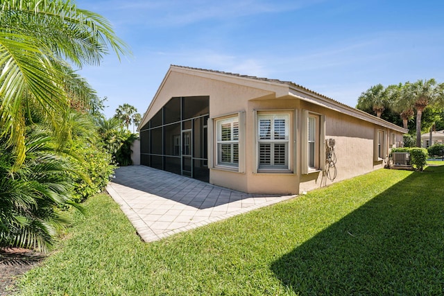 back of property with a sunroom, a patio area, a yard, and central AC