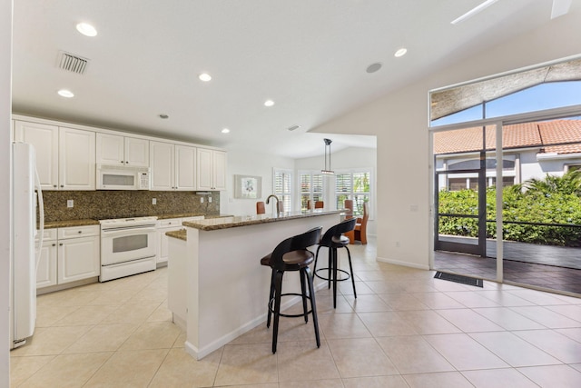 kitchen with white cabinetry, dark stone countertops, a wealth of natural light, and white appliances