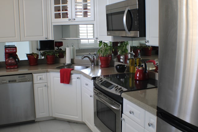 kitchen with appliances with stainless steel finishes, sink, white cabinetry, and light tile floors