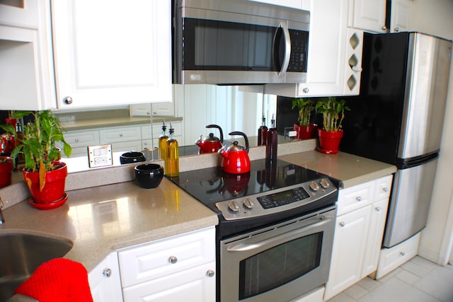 kitchen with appliances with stainless steel finishes, sink, white cabinetry, and light tile flooring