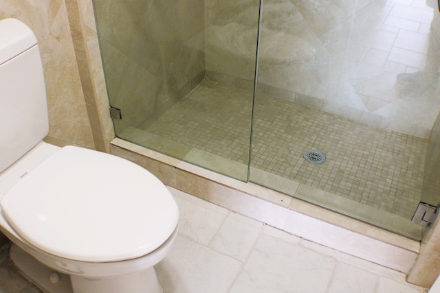 bathroom with toilet, tiled shower, and tile floors