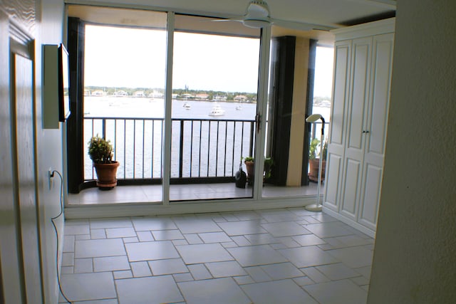 unfurnished room featuring ceiling fan, a water view, and light tile floors