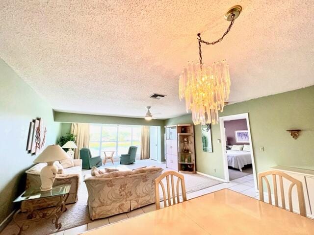 tiled dining space with ceiling fan with notable chandelier and a textured ceiling