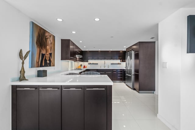 kitchen with stainless steel refrigerator, sink, dark brown cabinets, and light tile floors