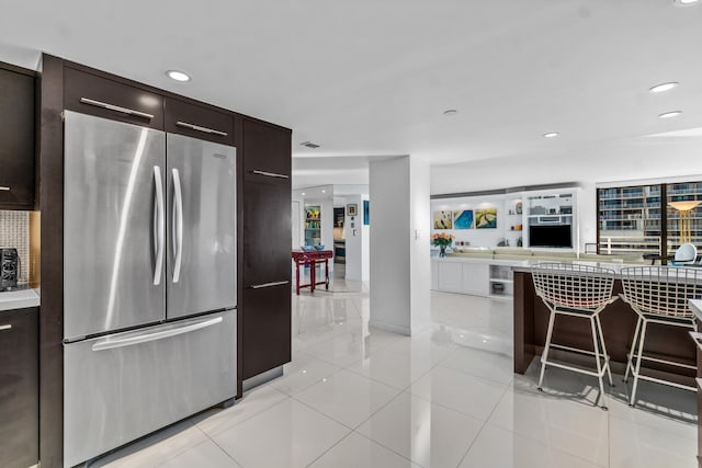 kitchen with stainless steel refrigerator, dark brown cabinetry, light tile floors, and a breakfast bar area