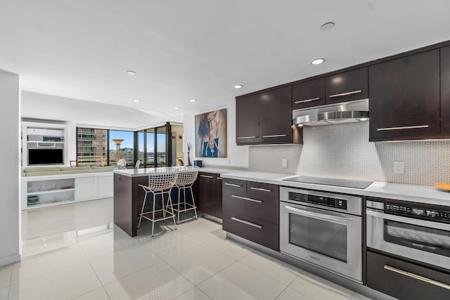 kitchen with black electric cooktop, dark brown cabinets, stainless steel oven, and a kitchen bar